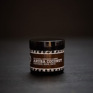 May include: A black jar with a white label that reads "100% NATURAL INGREDIENTS. ALWAYS. ARUBA COCONUT. MOISTURIZE. SHINE. GROW."