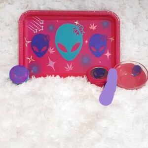 May include: Pink rolling tray with a teal alien design and gold glitter accents. The tray is surrounded by three small containers with alien designs.