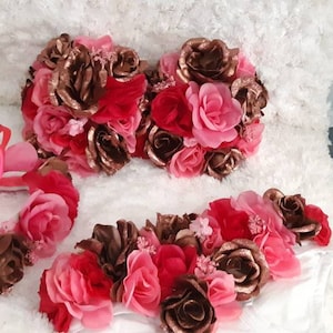 May include: Three pink and brown floral headbands with pink and brown flowers. The headbands are on a white fluffy surface.