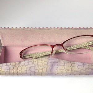 May include: A pink and white patterned glasses case with a red and silver pair of glasses inside.