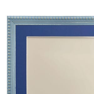 Pu&ograve; includere: Una cornice per foto blu chiaro con un passepartout blu scuro. La cornice ha un bordo perlato.
