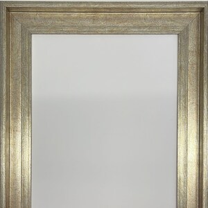 May include: A gold picture frame with a textured, wood-like finish. The frame has a simple, rectangular design and a wide border.