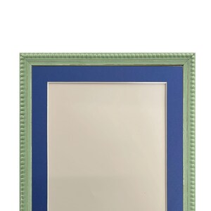 Puede incluir: Un marco de fotos verde con un borde interior azul. El marco tiene un borde decorativo con cuentas.