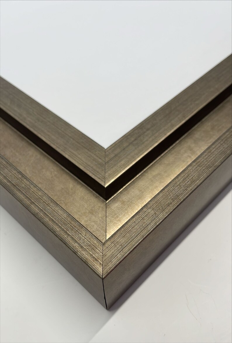 May include: Close-up of the corner of a double-layered picture frame. The frame is made of wood with a silver-toned finish. The frame has a slightly textured surface.