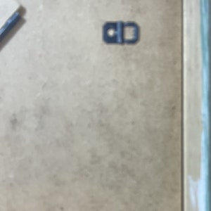May include: A close-up of a light brown picture frame with a black metal hanging hook.