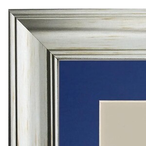 May include: Close-up of a silver picture frame with a white wood-grain finish. The frame has a dark blue mount and a cream-coloured inner mount.