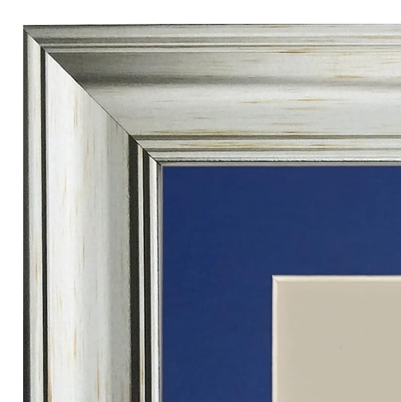 May include: Close-up of a silver picture frame with a white wood-grain finish. The frame has a dark blue mount and a cream-coloured inner mount.
