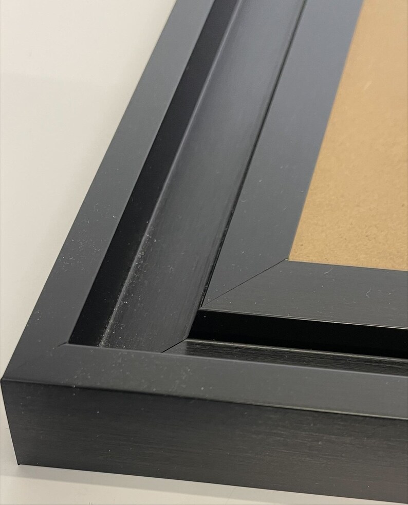 K&ouml;nnte beinhalten: Nahaufnahme der Ecke eines schwarzen Bilderrahmens. Der Rahmen hat ein zweilagiges Design mit einer glatten, leicht strukturierten Oberfl&auml;che.