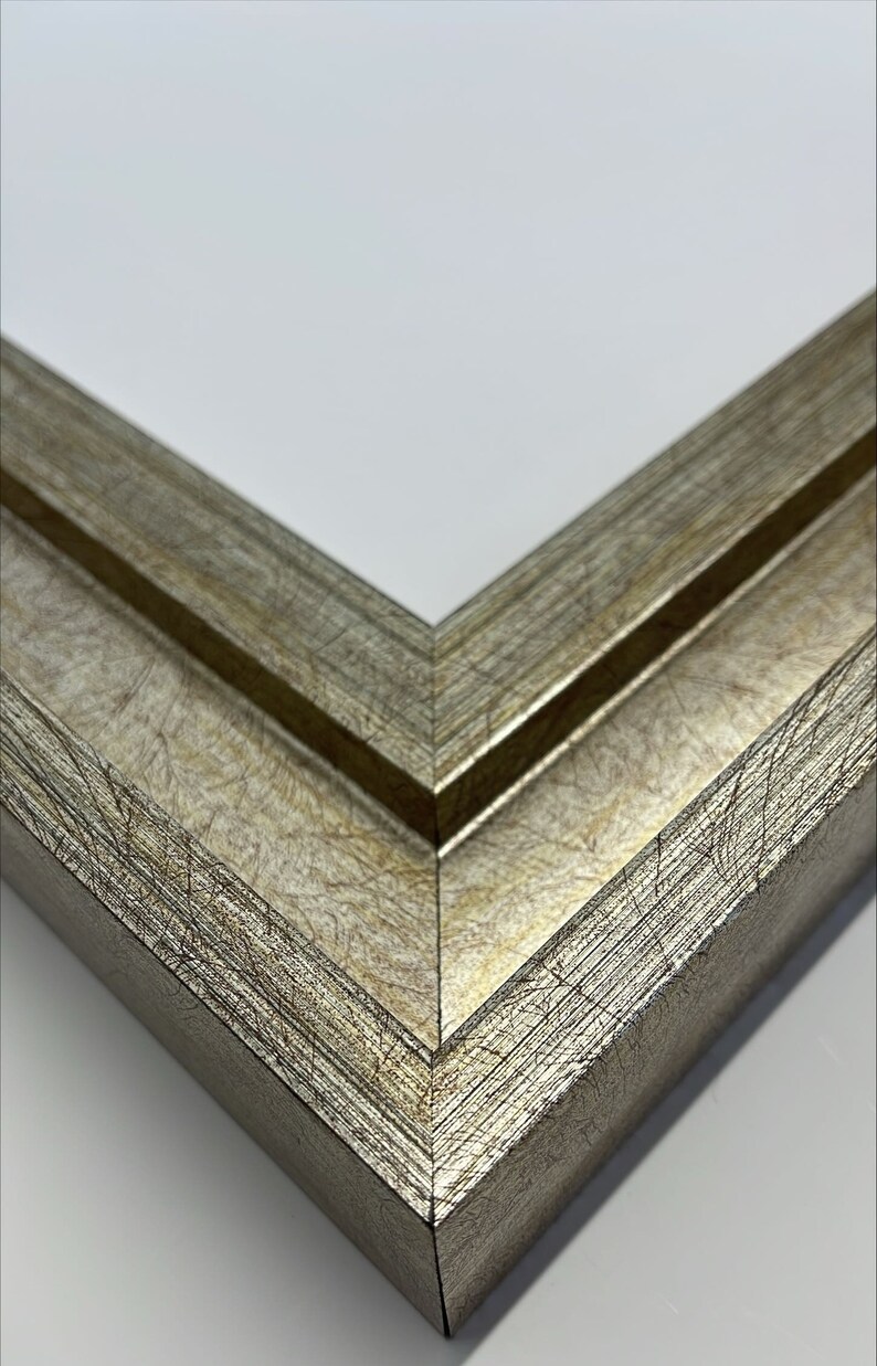 May include: Close-up of a corner of a silver picture frame with a wood grain texture. The frame has a double border.