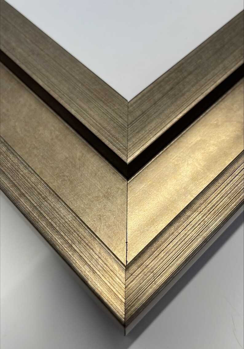 May include: Close-up of a corner of a double-layered picture frame with a gold finish. The frame has a textured surface and a beveled edge.