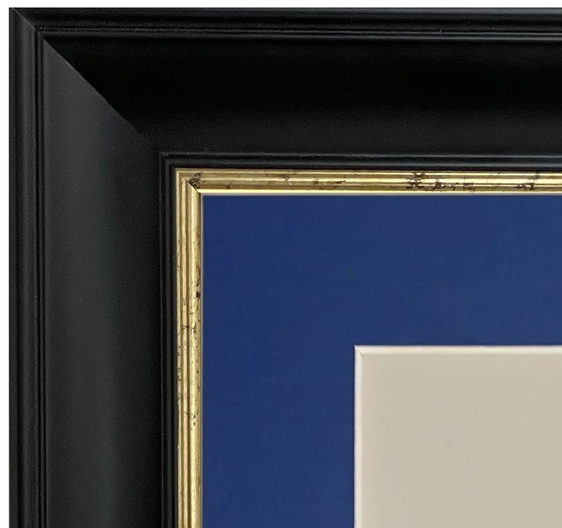 K&ouml;nnte beinhalten: Ein schwarzer Bilderrahmen mit goldener Verzierung und einem blauen Passepartout. Das Passepartout hat einen wei&szlig;en Innenrand.