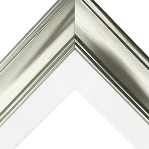 May include: Close-up of a corner of a silver picture frame with a white mat. The frame has a slightly distressed finish.