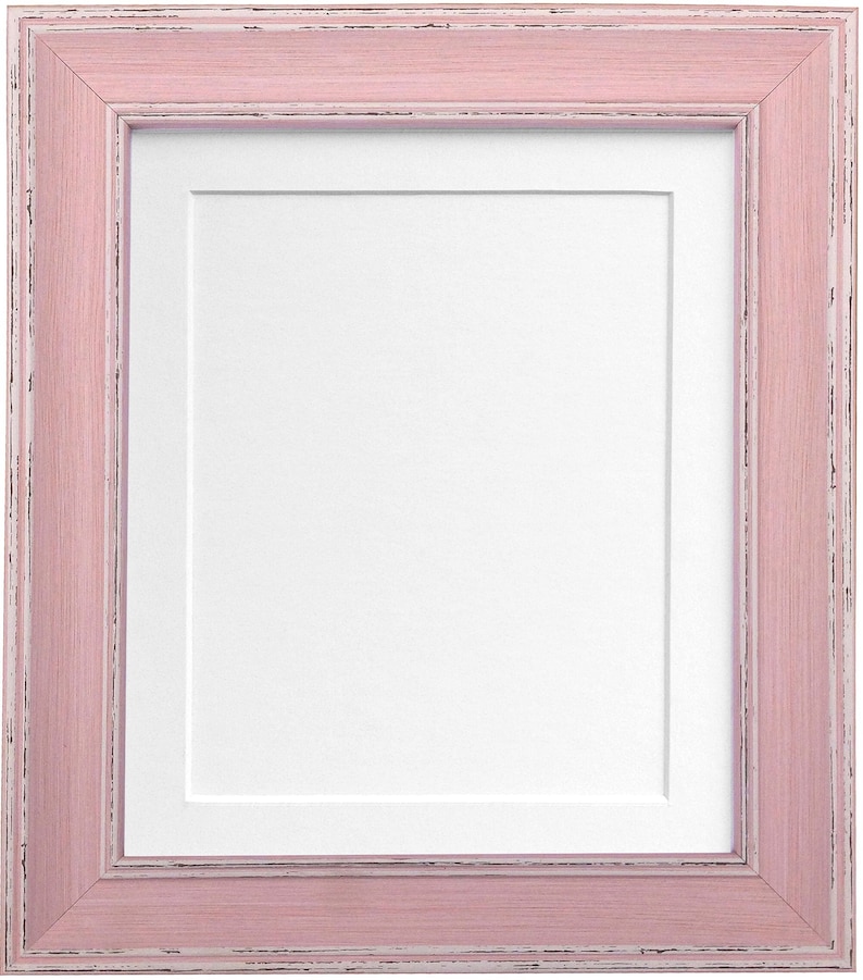 Puede incluir: Un marco de fotos rectangular con un acabado rosa claro envejecido. El marco tiene un paspart&uacute; blanco y una textura de veta de madera visible. Dise&ntilde;ado para contener una fotograf&iacute;a o una obra de arte.