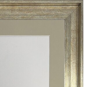 May include: A silver picture frame with a wide, ornate border and a beige mat. The frame has a distressed, antique look.