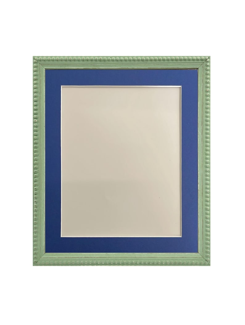 Puede incluir: Un marco de fotos verde con un borde interior azul. El marco tiene un borde decorativo con cuentas.