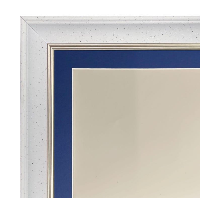 May include: Close-up of a white picture frame with a speckled texture. The frame has a silver inner border and a deep blue mount around a cream-coloured interior.