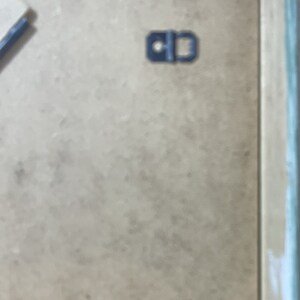 May include: A close-up of a light brown picture frame with a black metal hanging hook.