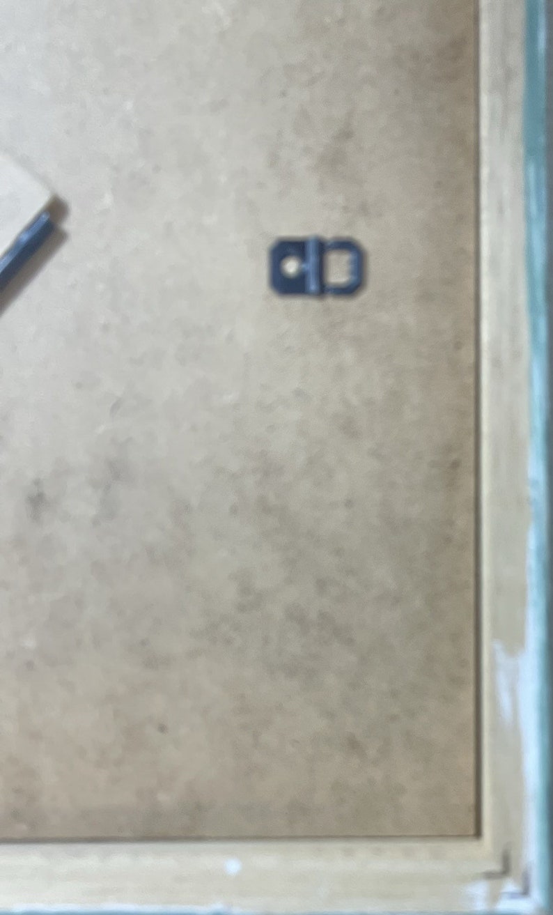 May include: A close-up of a light brown picture frame with a black metal hanging hook.
