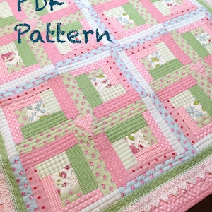 May include: A pink and green quilt with a white lace border. The quilt is made of various fabrics with floral and polka dot patterns. The text "PDF Pattern" is written in black on the quilt.