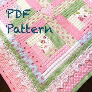May include: A PDF pattern for a quilt with a patchwork design featuring pink, green, and white fabrics. The quilt has a heart shape in the center and a lace trim around the edges. The text "PDF Pattern" is written in black on the quilt.