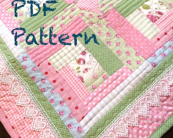May include: A PDF pattern for a quilt with a patchwork design featuring pink, green, and white fabrics. The quilt has a heart shape in the center and a lace trim around the edges. The text "PDF Pattern" is written in black on the quilt.