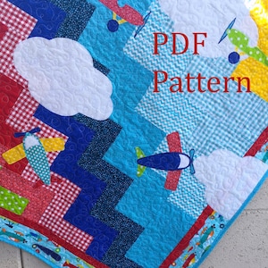 May include: A PDF pattern for a baby quilt featuring a blue, red, and yellow airplane design with white clouds. The quilt is made up of various geometric shapes and patterns.