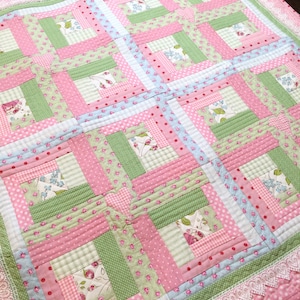 May include: A pink and green patchwork quilt with a white lace border. The quilt is made of various floral and geometric patterns.