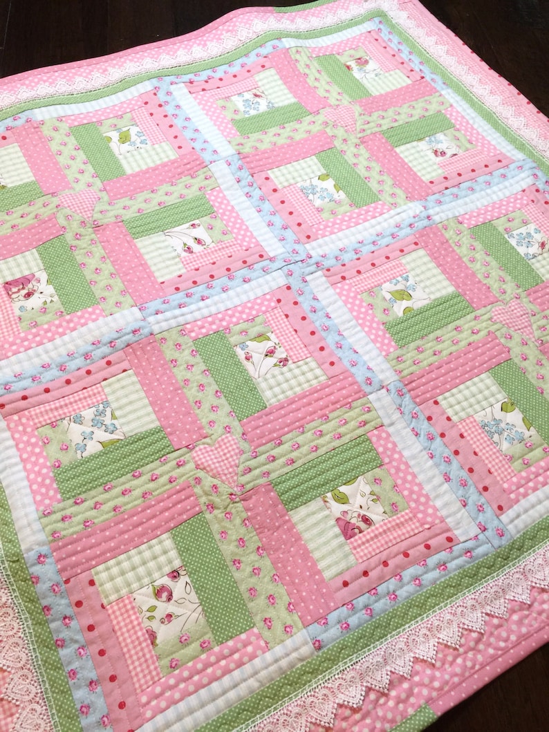 May include: A pink and green patchwork quilt with a white lace border. The quilt is made of various floral and geometric patterns.