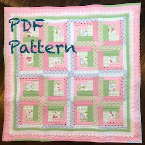 May include: A PDF pattern for a quilt with a log cabin design. The quilt is made with pink, green, and blue fabrics with floral and polka dot patterns. The quilt is edged with white lace.