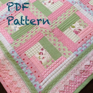 May include: A pink and green patchwork quilt with a white lace trim. The quilt is made of various fabrics with floral and polka dot patterns. The text "PDF Pattern" is written in black on the quilt.
