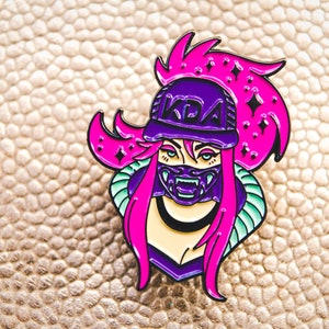 May include: A purple and pink enamel pin featuring a cartoon character with pink hair, a purple hat with the text "KDA" on it, and a purple and black mask.