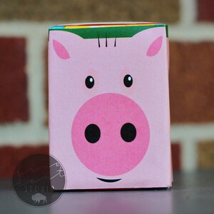 May include: A pink cardboard box with a cartoon pig face on the front. The pig has black eyes, a pink nose, and a black mouth.