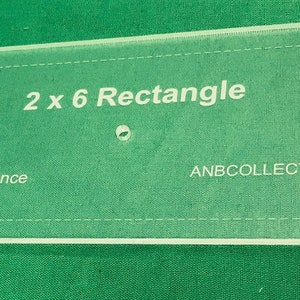 May include: A clear plastic sewing template for a 2 x 6 rectangle with 1/4 inch seam allowance. The template is labeled "2 x 6 Rectangle" and "ANBCOLLECTIBLES.COM".