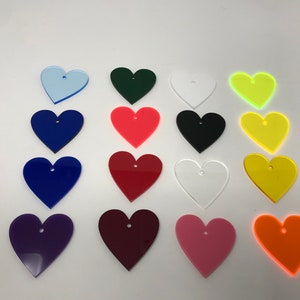 May include: Assortment of 16 heart-shaped acrylic blanks in various colors, including red, blue, green, yellow, orange, purple, pink, and white. Each heart has a small hole at the top.