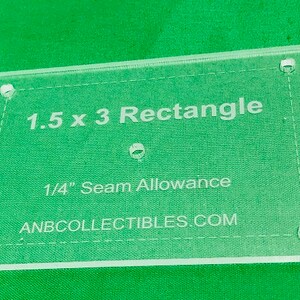May include: A clear plastic template for sewing projects. It is labeled "1.5 x 3 Rectangle" and "1/4" Seam Allowance" with the website "ANBCOLLECTIBLES.COM".
