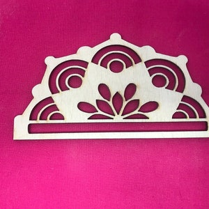 May include: A wooden napkin holder with a decorative design featuring a stylized flower and geometric shapes. The holder is made of light brown wood and has a simple, elegant design.