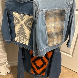 May include: Three denim jackets with different patterned fabric patches on the back. The patches are a white and gray geometric pattern, a plaid pattern, and an orange and black geometric pattern.