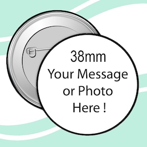 May include: A circular badge with a silver metal back and pin. The front features a white circle with the text "38mm Your Message or Photo Here!" in black. The badge is 3.8cm in diameter, against a light teal background.