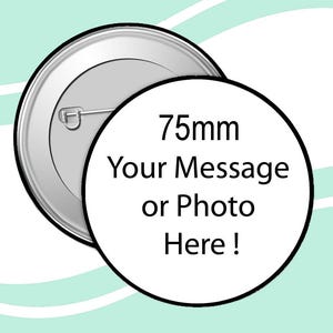 May include: A silver-coloured pin-back button with a safety pin on the back. The button has a white circular face with the text "75mm Your Message or Photo Here!" in black. The button is 7.5 cm in diameter.