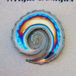 May include: A handcrafted, spiral-shaped art piece with iridescent colors of blue, orange, and gold. The artwork is set against a light gray background, with the text "Wright Designs" at the top. The spiral design is a unique, eye-catching decorative item.