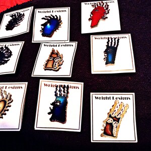 May include: Nine colorful enamel pins with a tribal design. Each pin features a different color and design. The pins are displayed on white cards with the text "Wright Designs".