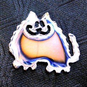 May include: A silver metal cat cutout with a blue and orange iridescent finish. The cat is sitting with its tail curled around its body.