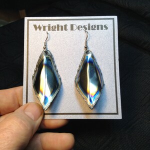 May include: A pair of iridescent silver teardrop-shaped earrings with a silver hook closure. The earrings are displayed on a white card with the text "Wright Designs".