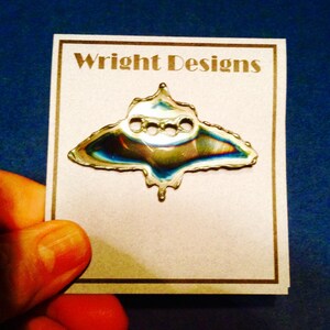 May include: A silver-colored metal pin in the shape of a stylized butterfly with a textured surface. The pin is displayed on a white card with the text "Wright Designs" printed in black.
