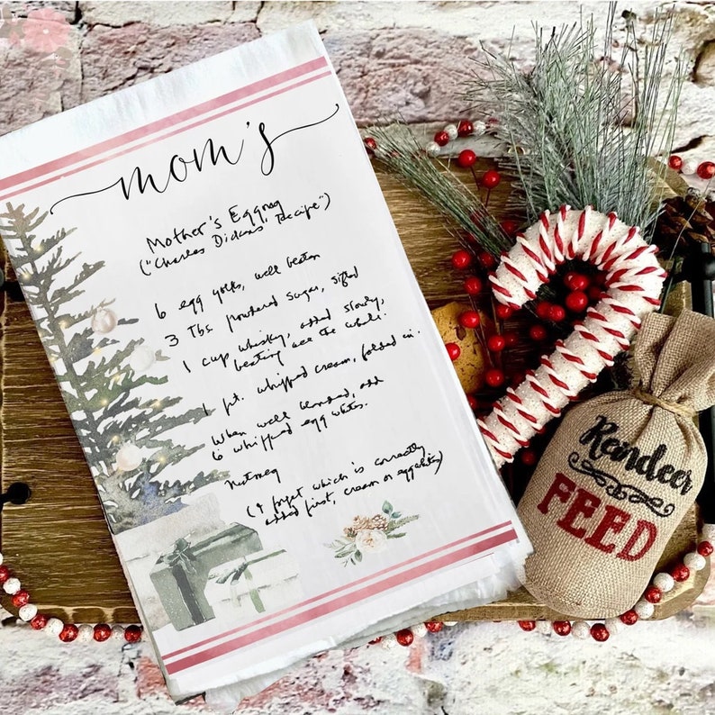 May include: A printable kitchen towel with a handwritten recipe for "Mother's Eggnog" on a rustic wooden background with a red and white candy cane and a burlap bag with the words "Reindeer Feed" printed on it.