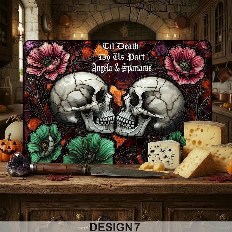 May include: A cutting board with a skull design and the text "Til Death Do Us Part Angela & Spartacus." The board features two skulls, flowers, and a knife. Various cheeses are arranged on a wooden surface.