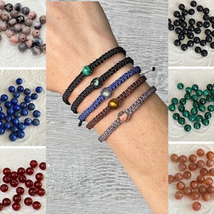 Peut inclure: Cinq bracelets avec des perles de pierres précieuses de différentes couleurs. Les bracelets sont faits de cordons noirs, bleus, bruns et gris. Les perles sont en malachite, œil de tigre, labradorite, cornaline et lapis-lazuli.
