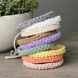 May include: A stack of eight crocheted bracelets in various pastel colours, including grey, white, beige, brown, lavender, green, yellow, orange, and pink.