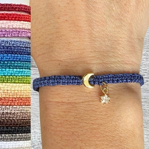 May include: A navy blue braided bracelet with a gold crescent moon charm and a gold star charm with a clear crystal centre.
