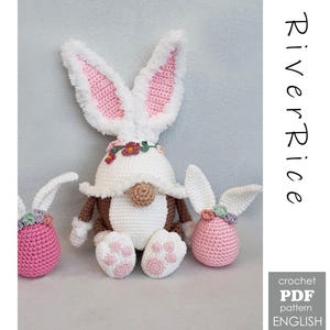 May include: Crocheted Easter bunny gnome with white fur-trimmed ears, pink inner ears, and a floral crown. The gnome has a white hat, brown arms, and white feet with pink paw prints. Two smaller bunny-shaped ornaments are also present.